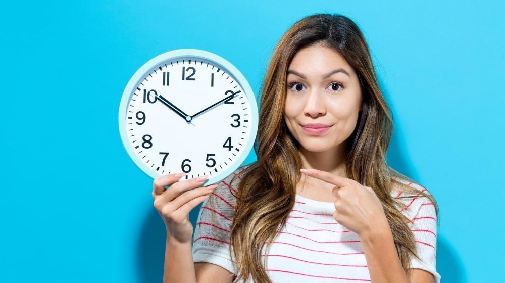 a girl hoding a clock and pointing at it with blue background | We Can Now Turn Back the Biological Clock: 5 Advantages of Epigenetics | feature
