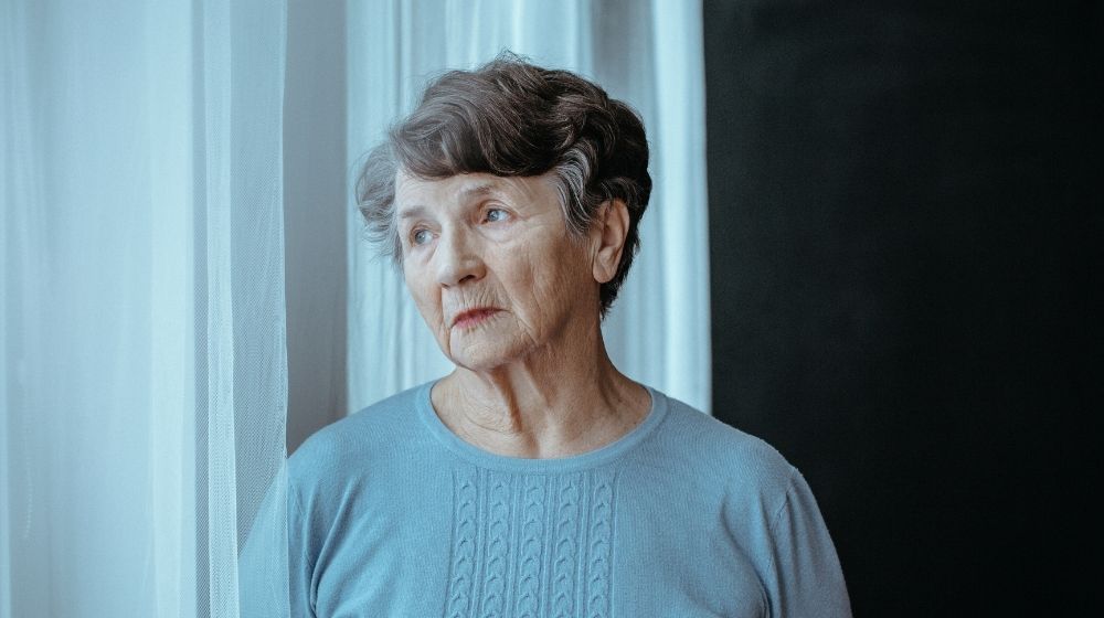 an old lady is standing at the curtain and confusingly looking outside | Feature | Alzheimer's Disease: How Epigenetics Is Changing What We Know
