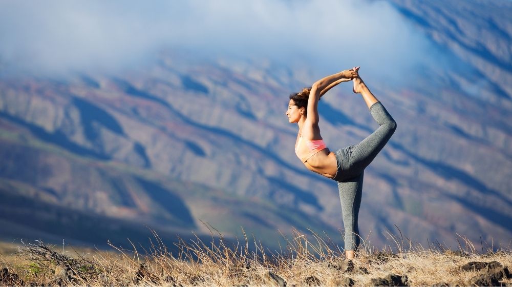 a woman is doing a yoga posing with the moutain on the background - | The Important Link Between Yoga and Epigenetics | Feature