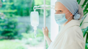 female-chemotherapy-patient-wearing-mask-looking-out-window-with-IV-drip | P16INK4a Expression Determines Link Between Chemotherapy and Accelerated Aging in Cancer Survivors | feature