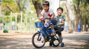 2 Latin children riding a bike on the school background | Feature | Blog - Socioeconomic Disadvantage Accelerates Biological Aging in Children