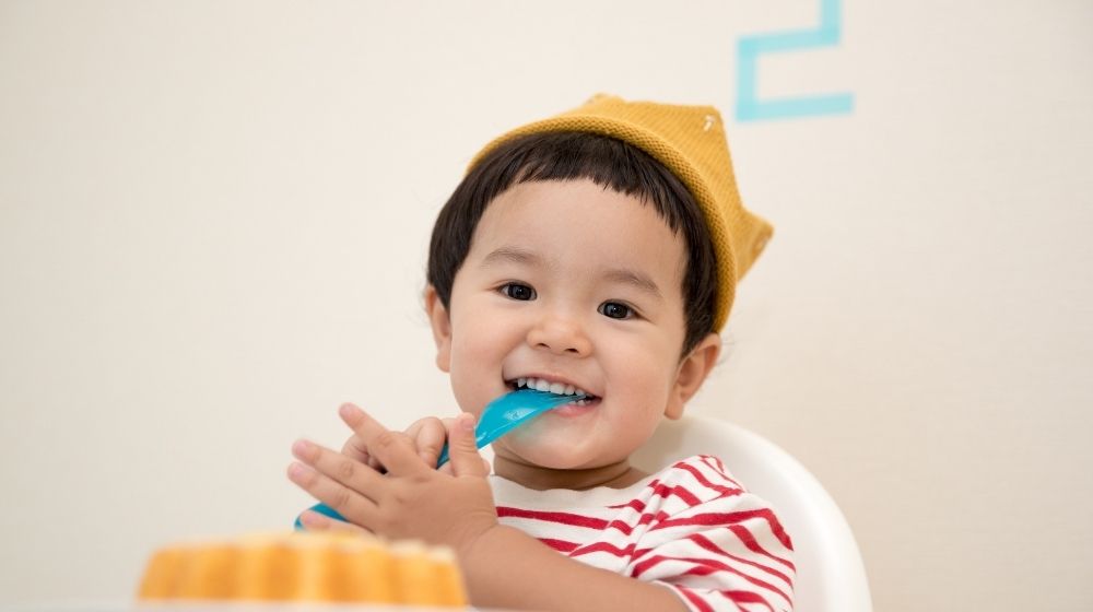 a toddler wearing striped shirt putting the spoon on his mouth with the cake in the front | Feature | The Link Between Epigenetics and Social Factors